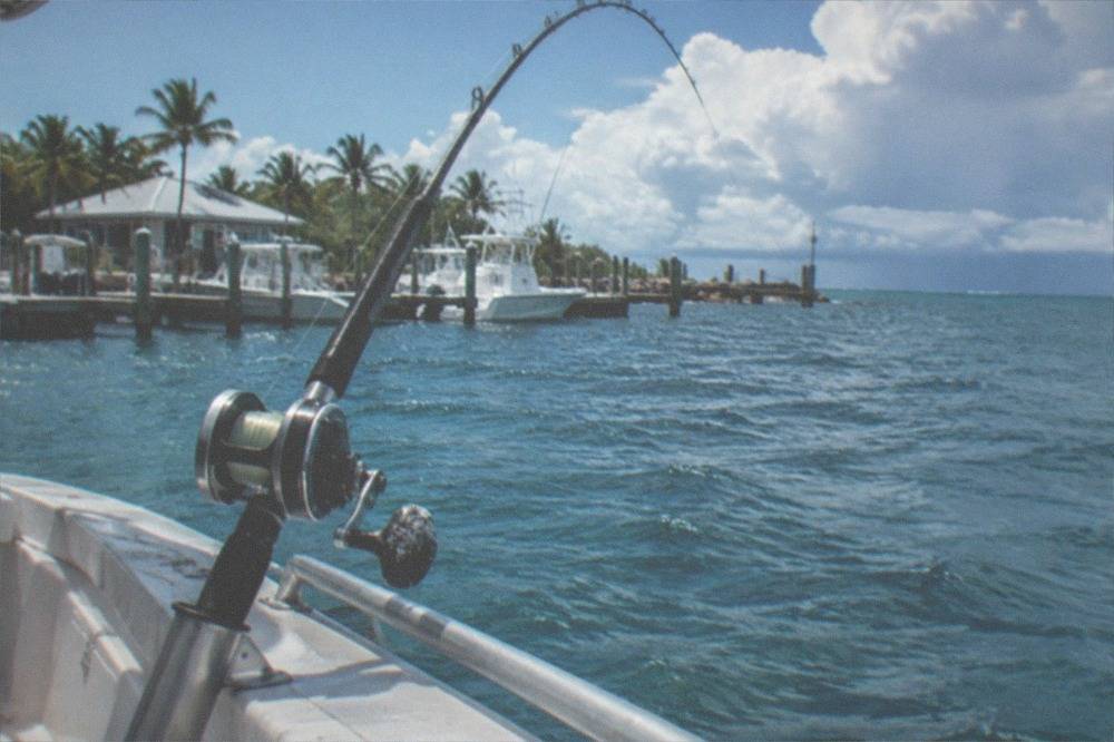 A fishing rod bent in a rod holder on a boat deck with deep blue open water beyond the rail.