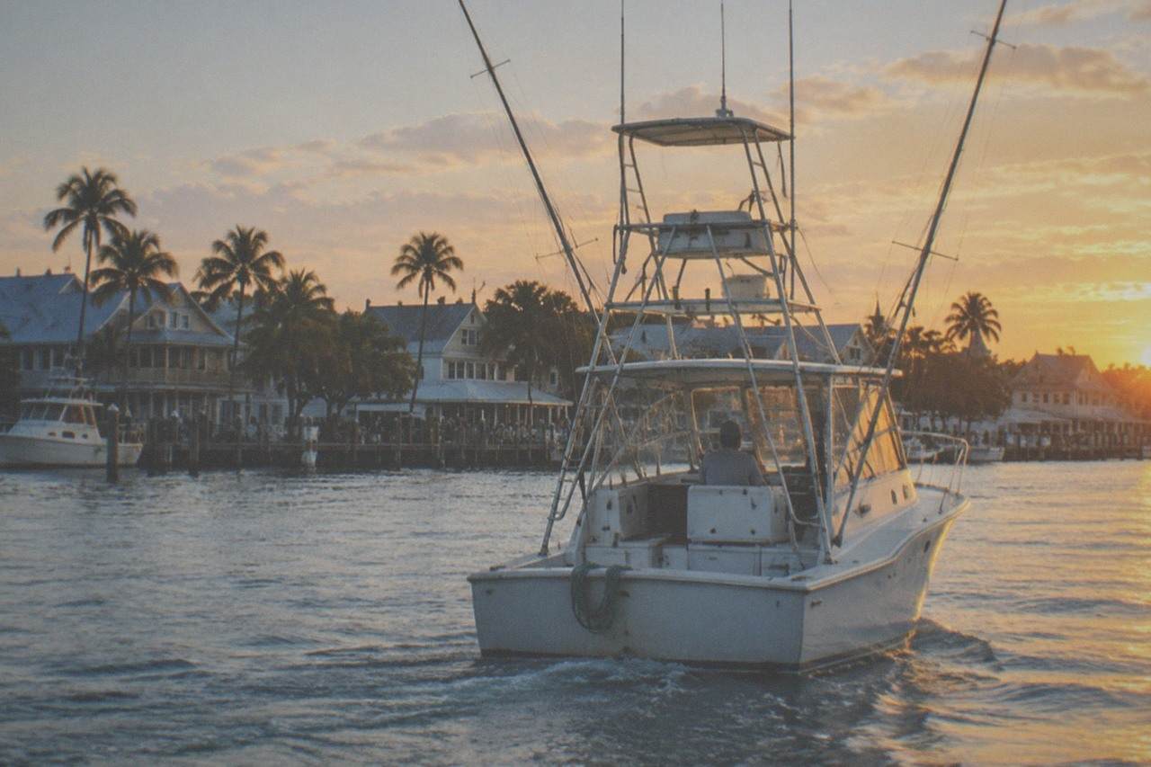 A vintage-style sportfishing boat cruising calm blue water off a tropical island coastline at golden hour.