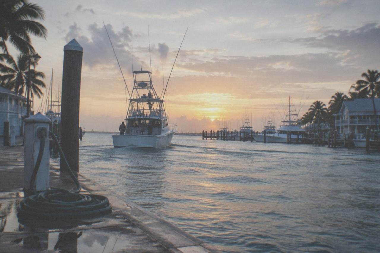 A fishing charter boat heading out from Key West toward open water at sunrise