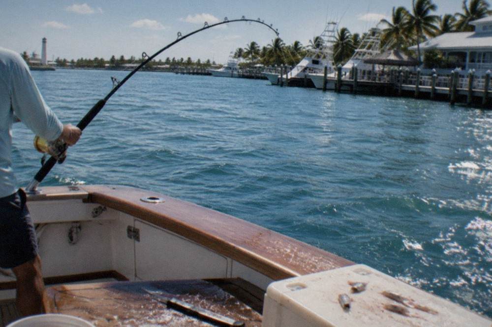 A fishing rod bent hard with a fish on the line, seen from the deck of a sportfisher in open water