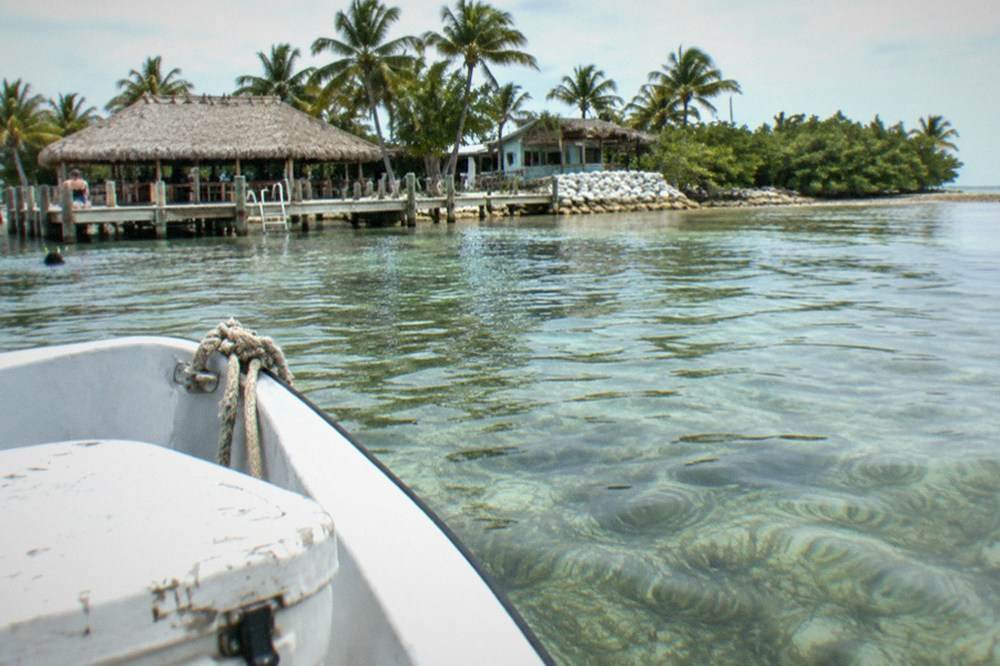A fishing boat anchored over a shallow reef flat with visible coral and seagrass