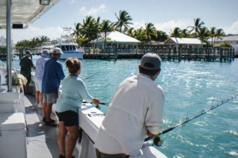 A wide party fishing boat underway off Key West with anglers spaced along both rails, lines down and rods bending under a clear morning sky