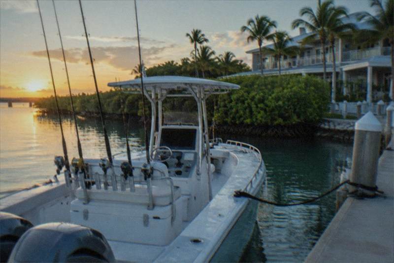 A private charter boat idling at a Key West dock in early light, rods rigged in the holders and the deck cleared for a small group heading out alone