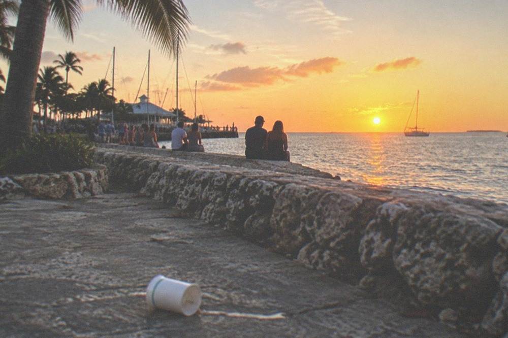A public plaza and pier at sunset with a crowd gathered along the seawall facing open water