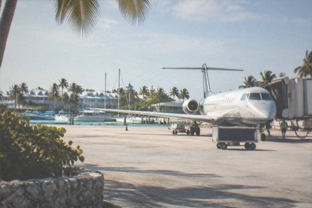 A small airport runway beside palm trees with a passenger plane at the gate