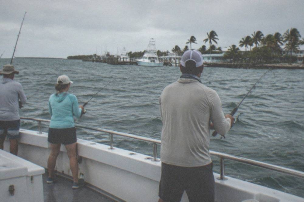 A small group of anglers reeling in lines along the rail of a charter boat in open water
