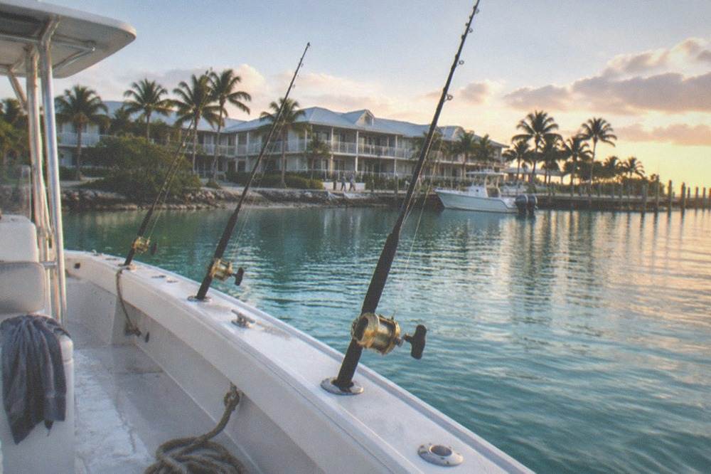 A charter boat anchored over calm turquoise water with fishing rods leaning in holders