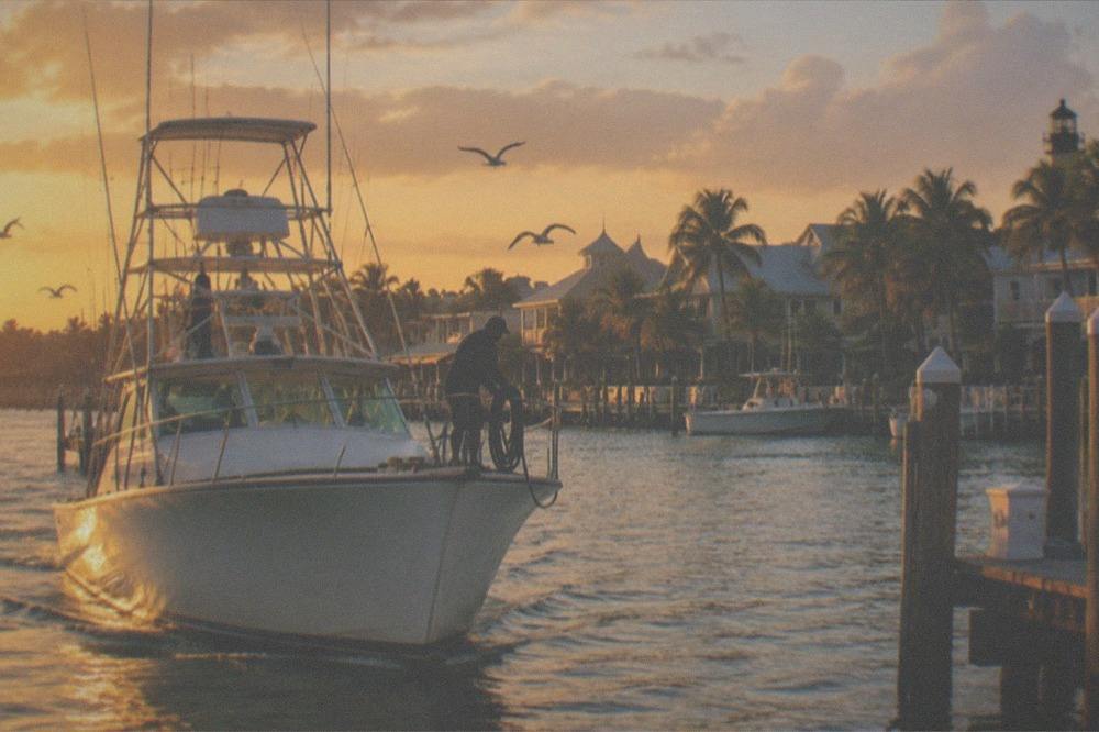 A fishing charter boat returning to a Key West harbor at golden hour with the skyline behind it