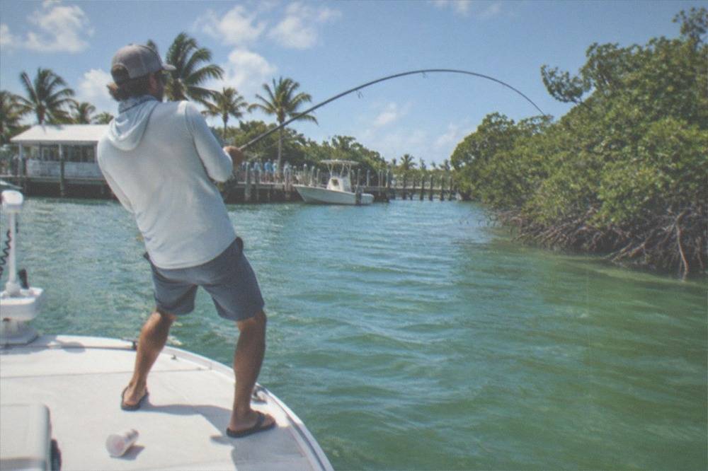 A fishing rod bent over the gunwale of a flats skiff in shallow green water