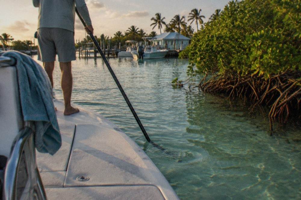 Shallow mangrove-lined flat with a bay boat poling across turquoise water