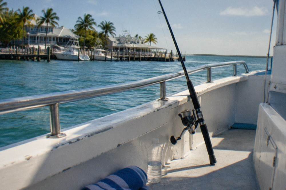 A fishing rod leaning against the railing of a boat with open water and a clear sky behind it
