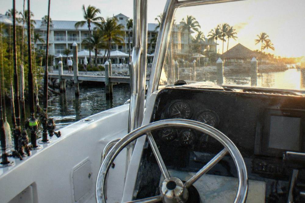 A boat console and steering wheel with fishing rods racked along the side and blue sky above