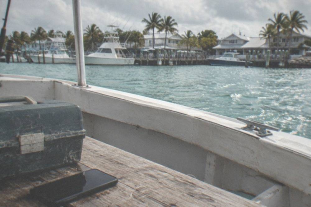 A smartphone and fishing tackle box resting on a wooden boat bench with water in the background