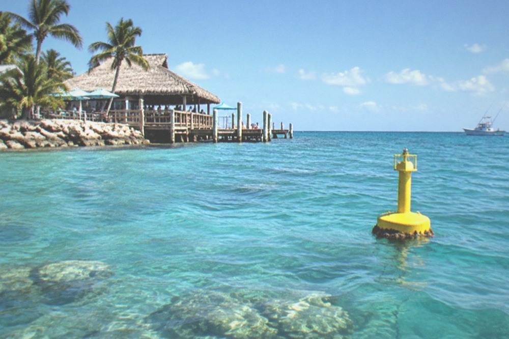 A yellow sanctuary buoy floating on clear turquoise water with a fishing boat in the distance