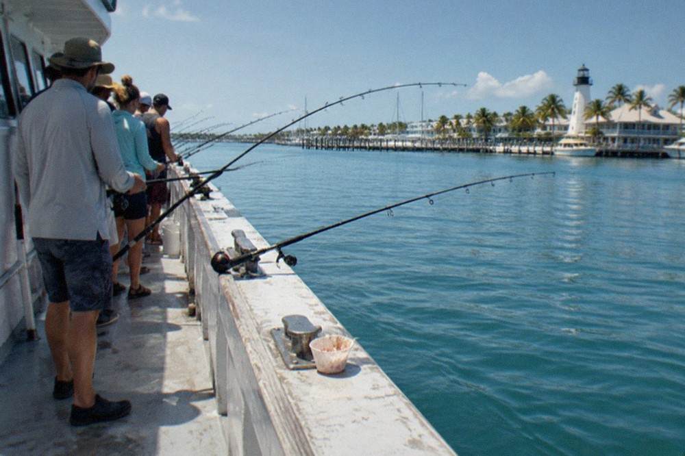 Anglers standing shoulder to shoulder along the rail of a large party fishing boat with bent rods over calm blue water
