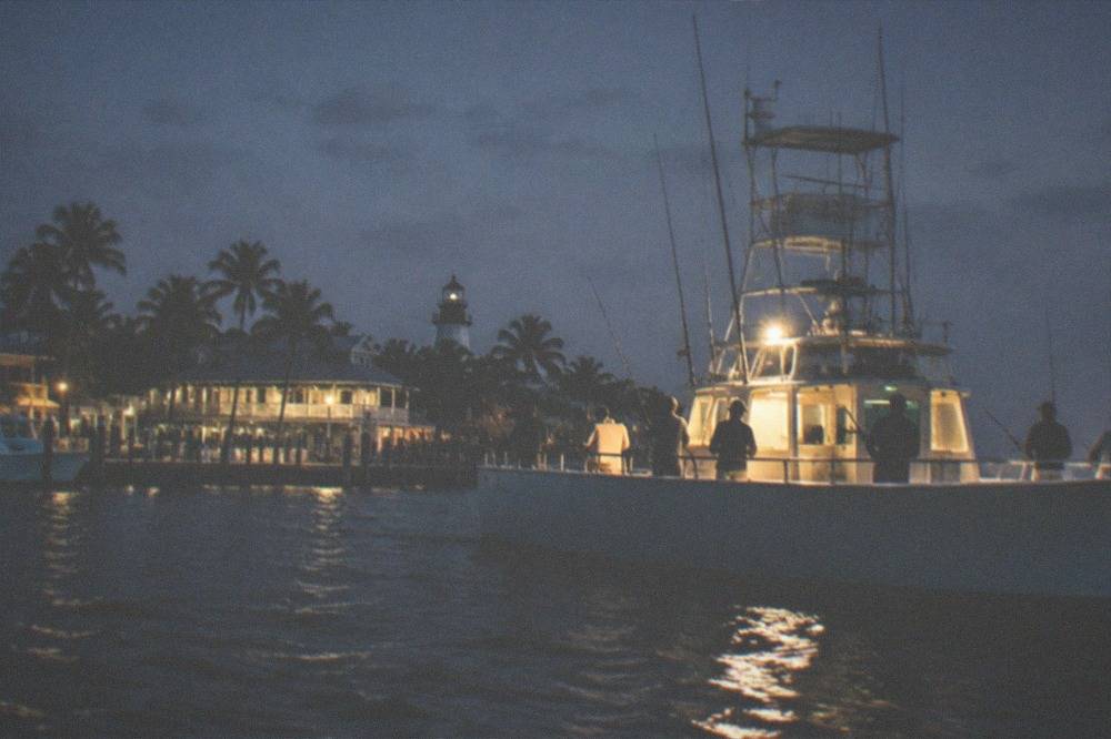 A party fishing boat lit from within fishing after dark with anglers' silhouettes along the rail