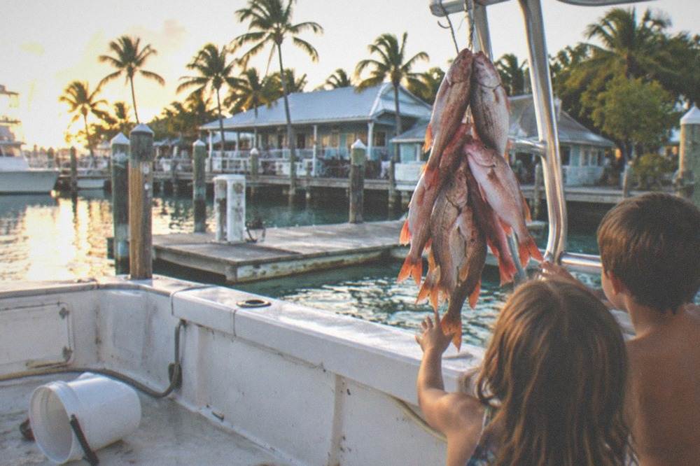 A family with children holding up a stringer of snapper on the deck of a party fishing boat