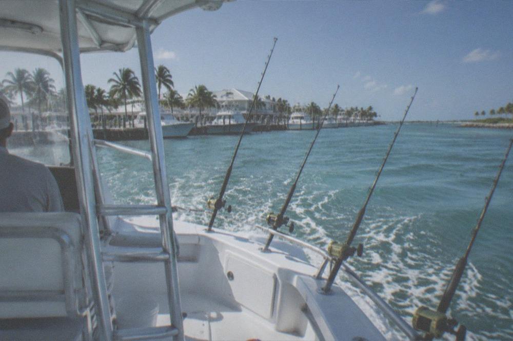 A small offshore fishing boat running out past a reef with rods trolling in the outriggers