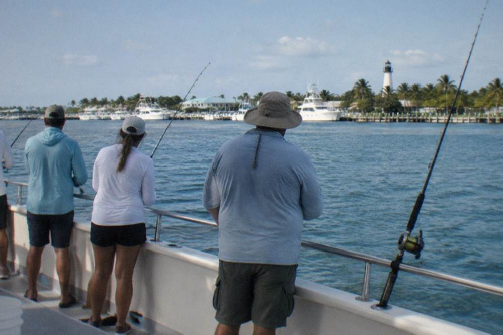 Anglers fishing side by side along the rail of a large party boat on calm blue water near Key West