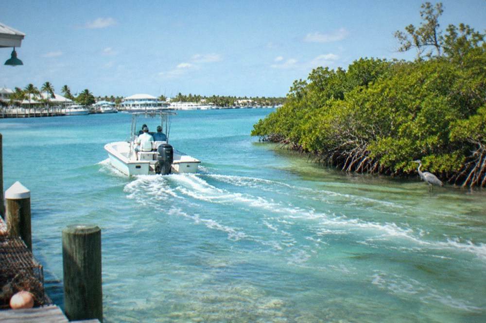 A small private charter boat cruising over shallow turquoise water toward open sea