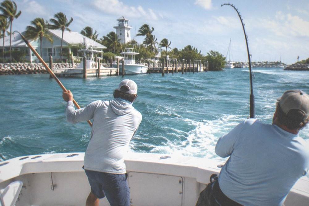 Deckhand gaffing a fish at the stern of a charter boat while an angler holds the rod