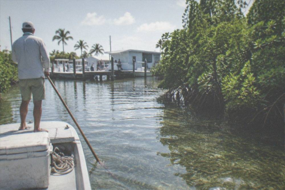 A flats skiff polling across shallow clear water among mangrove islands near Key West