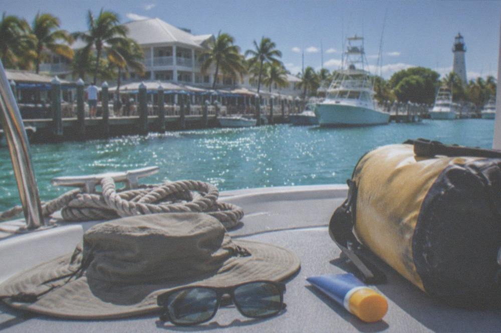 A hat, sunglasses and sunscreen tube laid out on a boat deck beside a dry bag